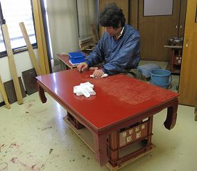 漆塗り工程、朱塗り（中塗り）の表面を丁寧に水砥ぎしている座卓の様子です